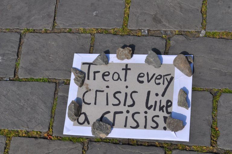 Demoschild: Treat every crisis like a crisis