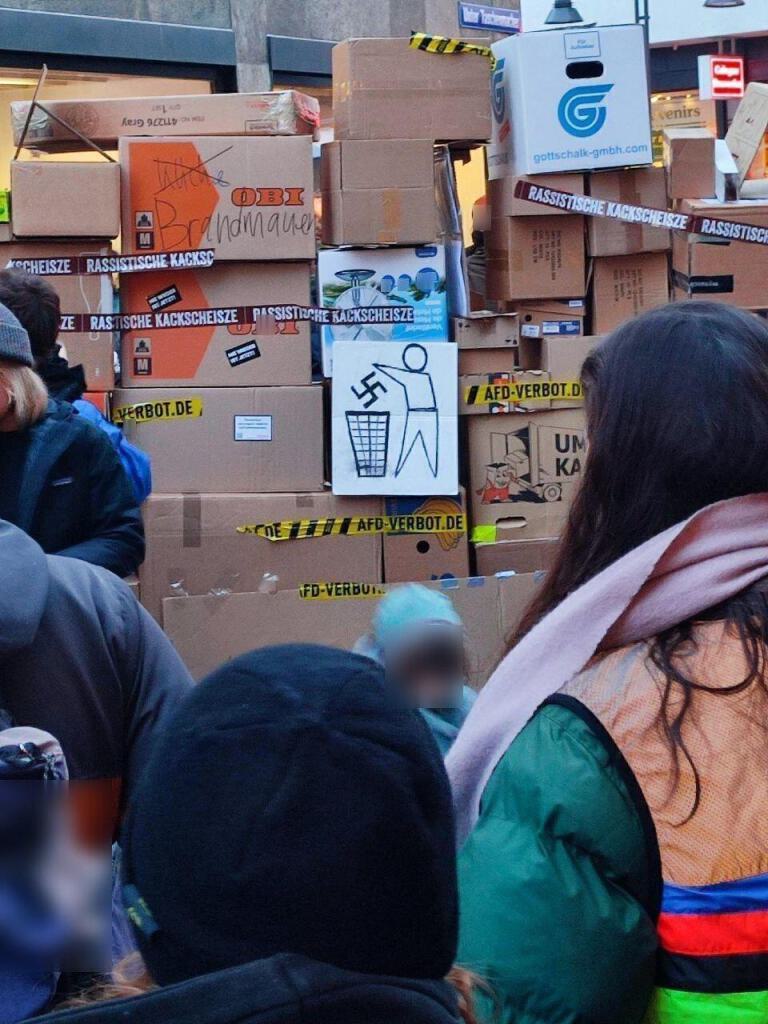 Aus Kartons errichtete symbolische Brandmauer gegen Rechts vor der Kölner CDU Zentrale. Mit der klaren Forderung nach einem AfD-verbot. Im Vordergrund stehen Menschen mit dem Rücken zur Kamera