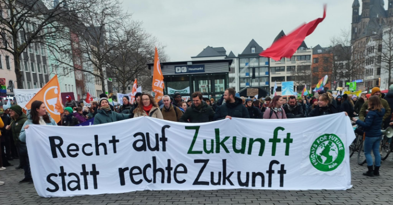 Klimastreik der Fridays for Future in Köln am 14.02.25. Eine Menschenmenge demonstriert auf dem Heumarkt. Im Vordergrund halten mehrere Personen ein großes, weißes Banner mit der Aufschrift "Recht auf Zukunft statt rechte Zukunft". Im Hintergrund sind weitere Demonstranten mit Flaggen und Schildern zu sehen.